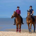 2 horses and their riders on a sunny beach as part of luxury riding holidays.